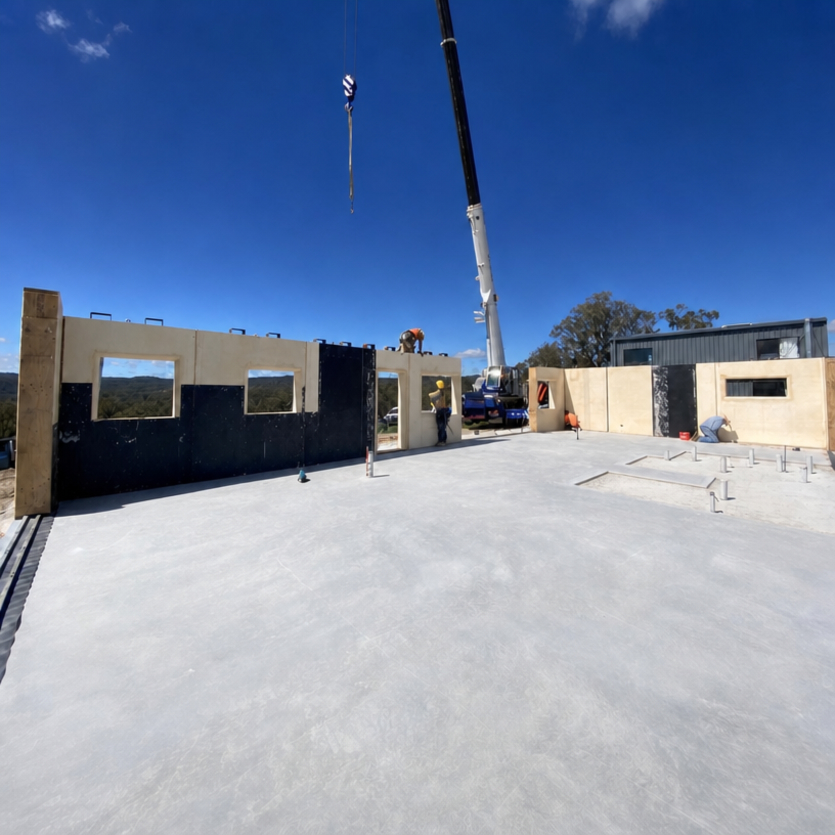 Crane lifting prefabricated Viva Panels into place on a concrete slab with rural views